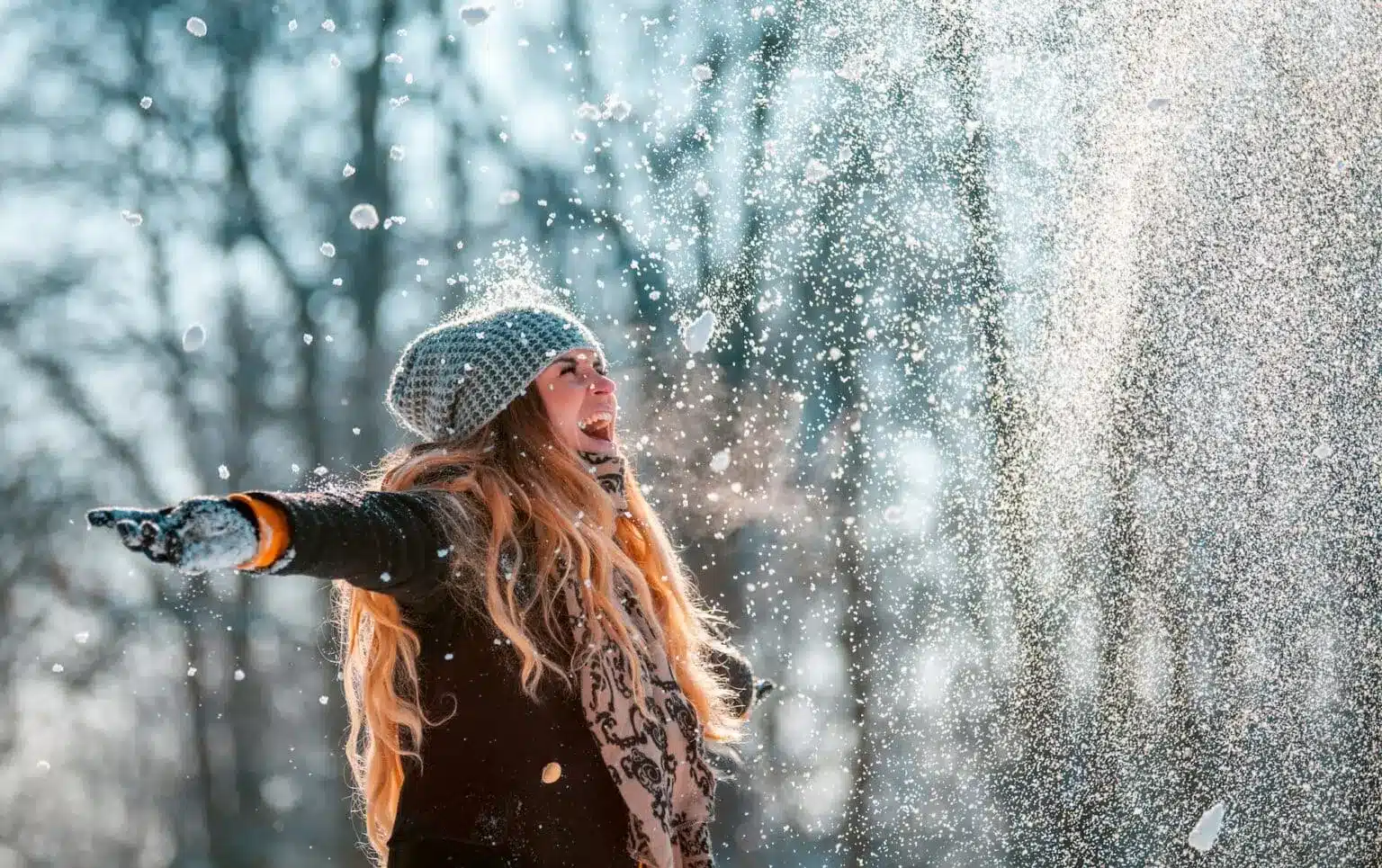 Woman in winter clothing enjoying falling snow with arms outstretched